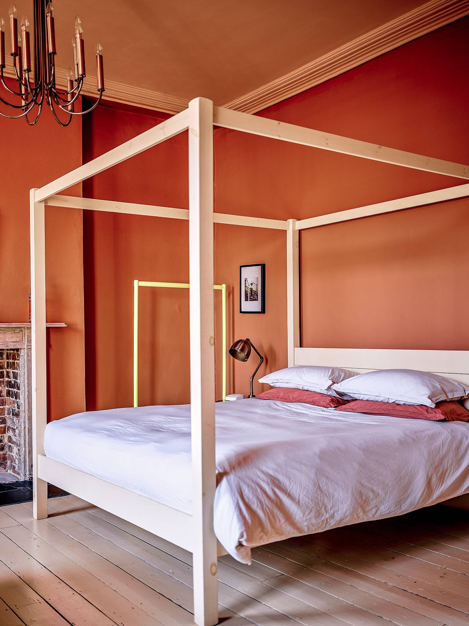 Spacious terracotta orange bedroom featuring a timber four-poster bed frame and white linens, ideal for mattress and sleepwear ads, Love Locations.