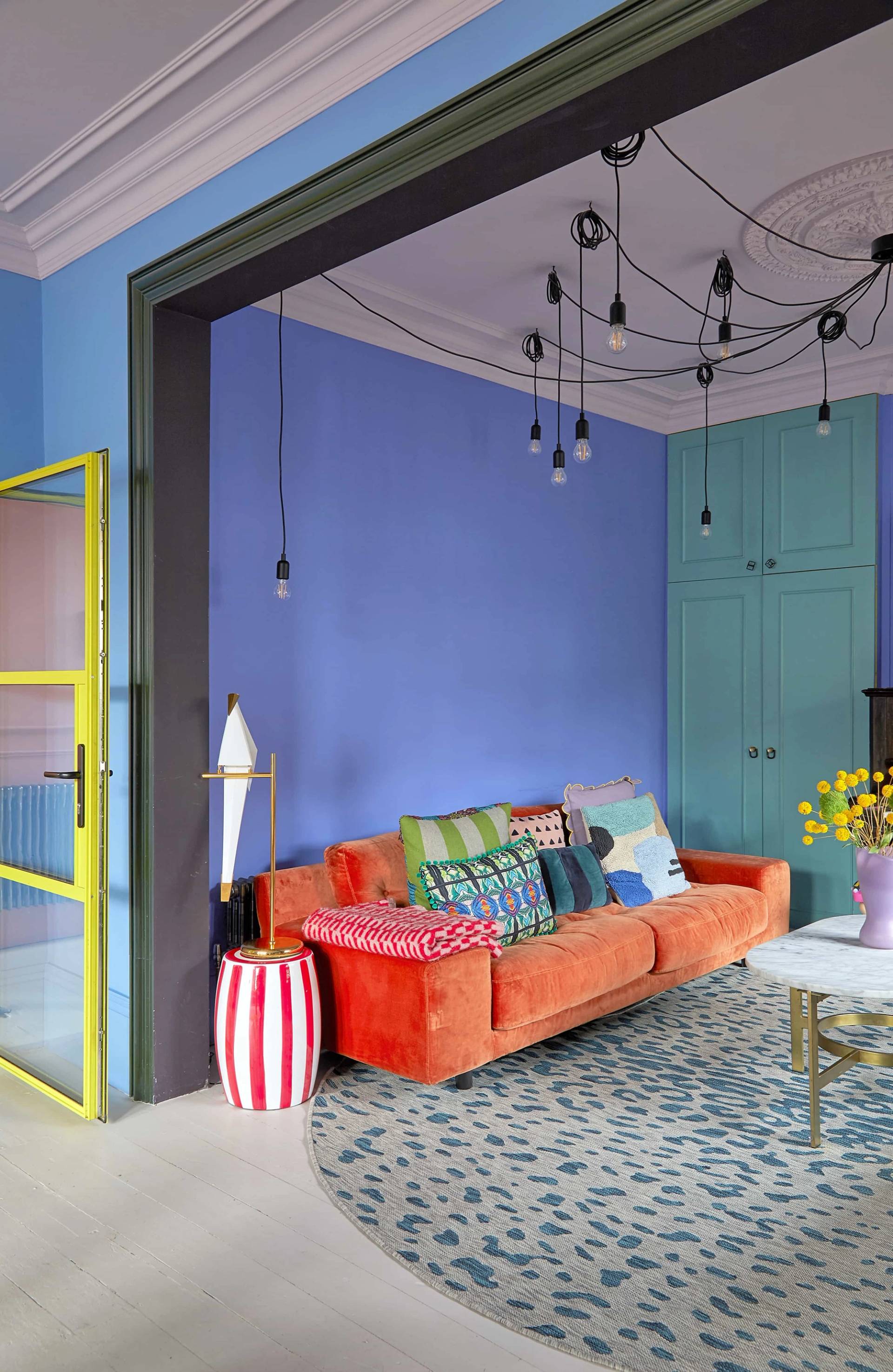 Vibrant reception room featuring an orange sofa with colorful cushions set under a spider chandelier light, Love Locations SE6.