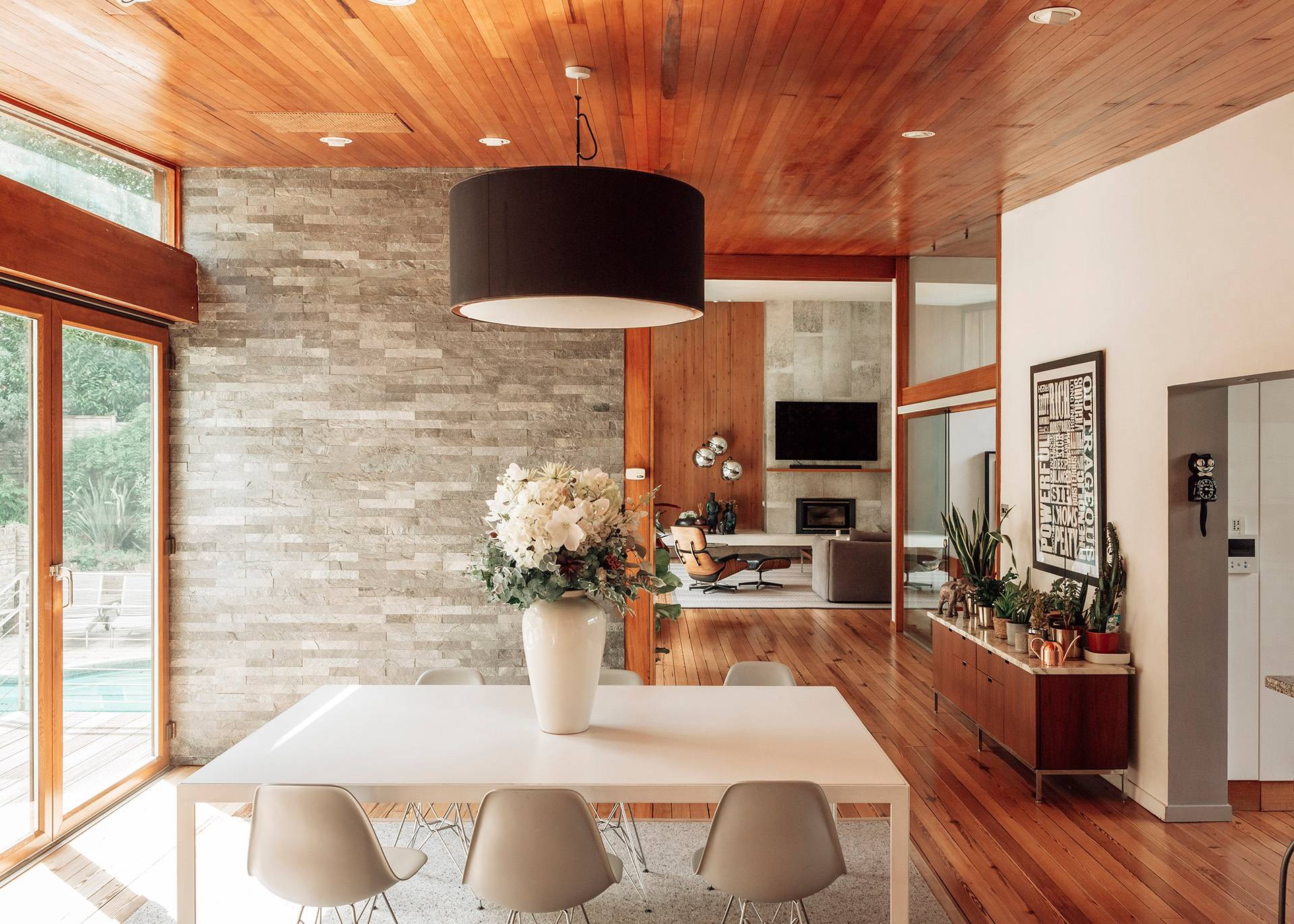 Mid-century dining area featuring a white table, Eames-style chairs, and a stunning backdrop of open wood-framed windows, Love Locations.