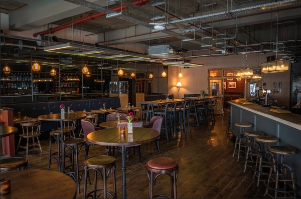 Atmospheric restaurant interior setup showing round wooden high-top tables, bar stools, and warm statement pendant lighting, ideal for hospitality lifestyle photography, Love Locations.