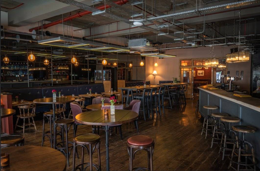 Atmospheric restaurant interior setup showing round wooden high-top tables, bar stools, and warm statement pendant lighting, ideal for hospitality lifestyle photography, Love Locations.