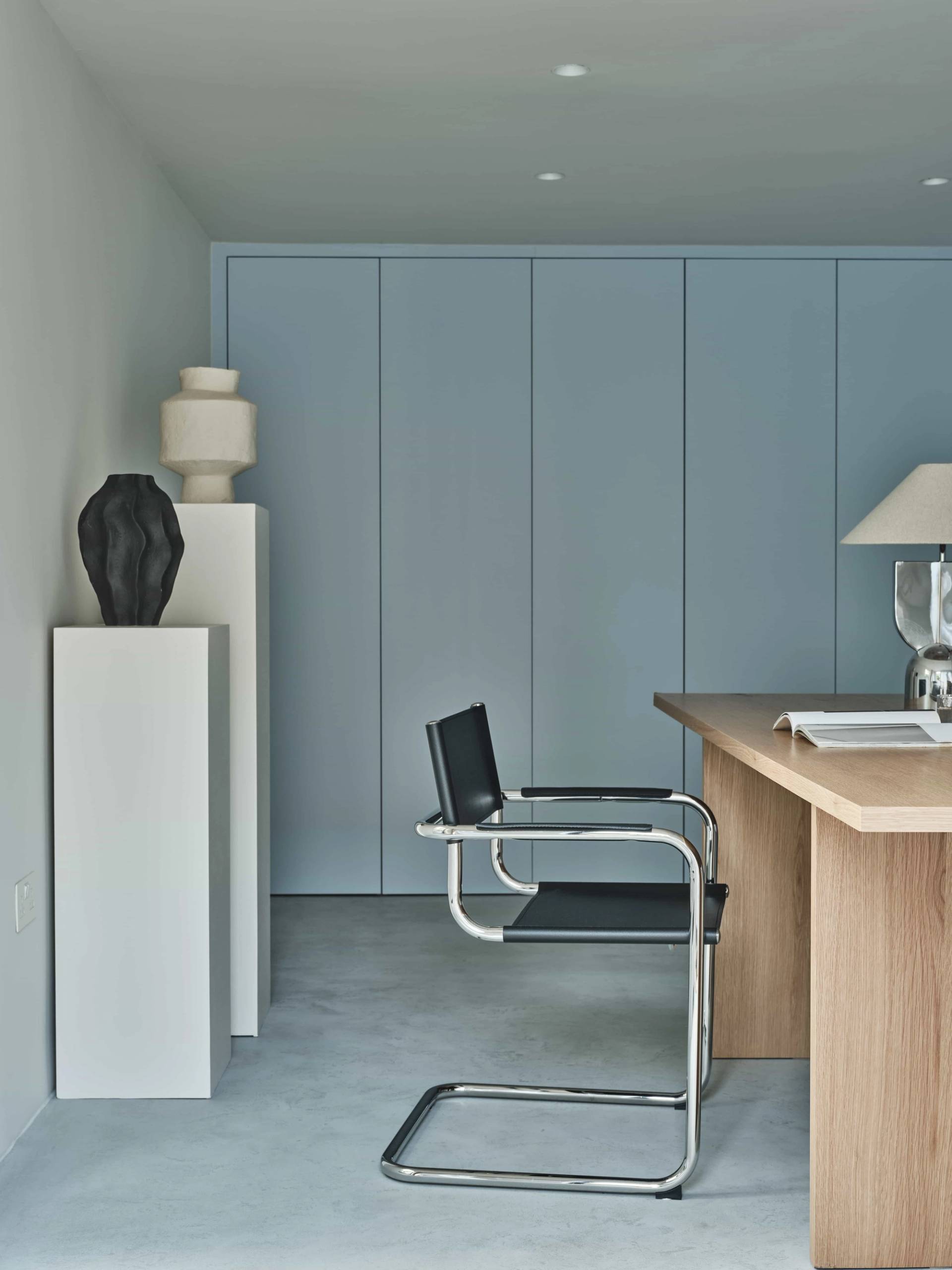 Powder blue fitted wardrobe storage wall with white plinth display stands and chrome chair in a garden office studio, Love Locations E4.