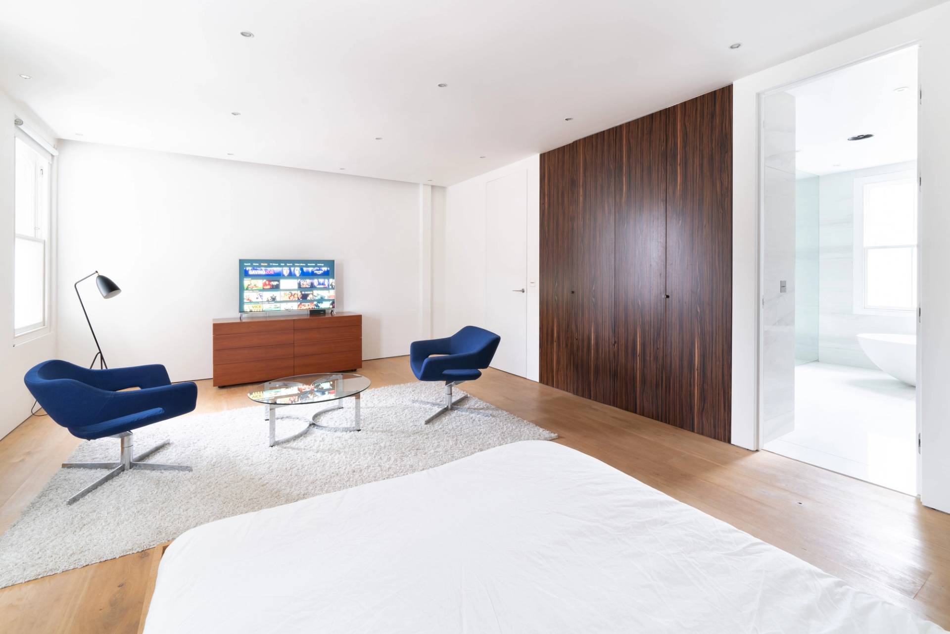 Light-filled master bedroom with low timber bed frame, dark wardrobe doors, and ensuite access, Love Locations SW6.