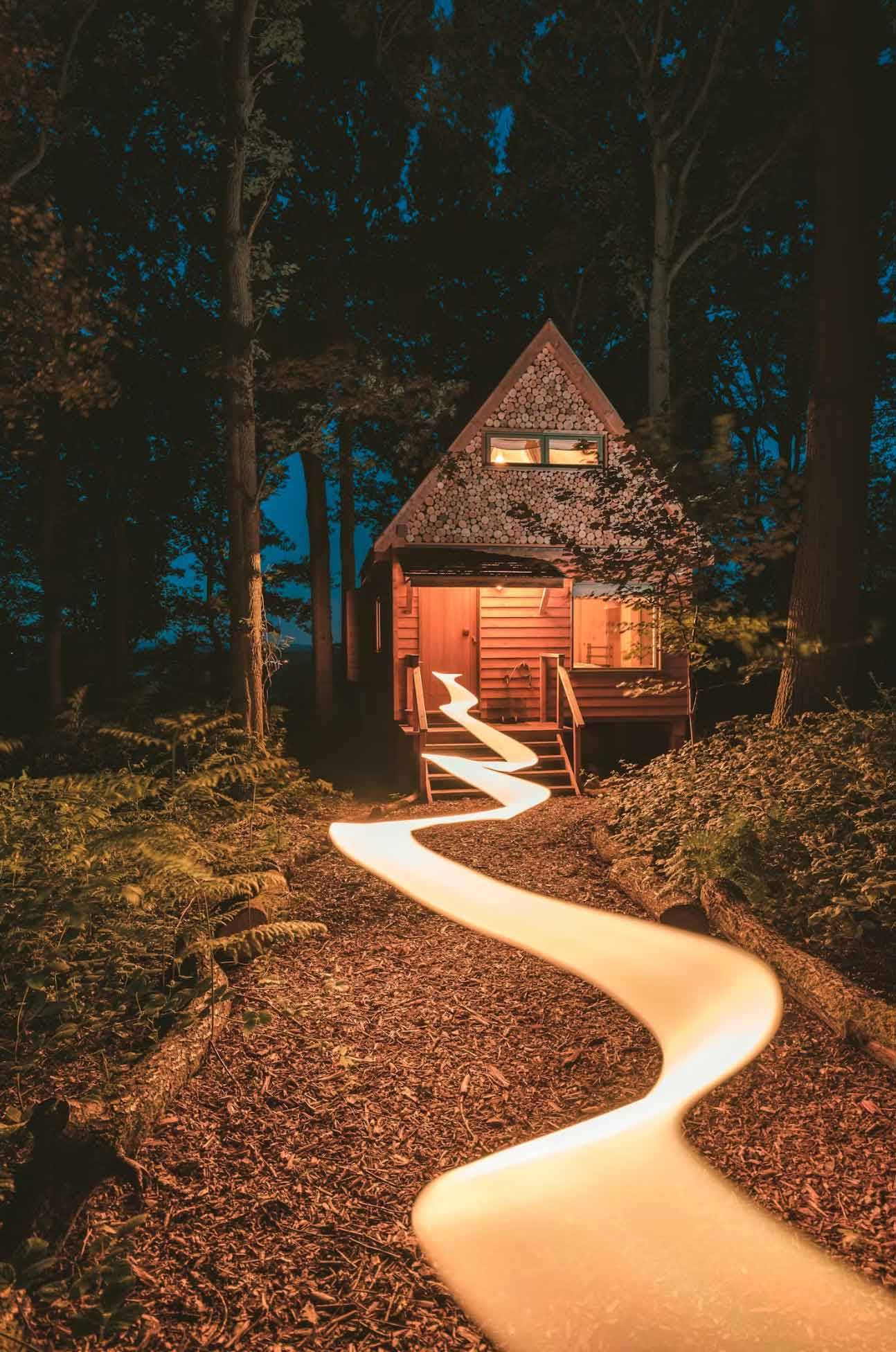 Stunning night photography set showing a glowing wooden cabin with a beautifully lit winding walkway trail cutting through the dark woods, Love Locations.