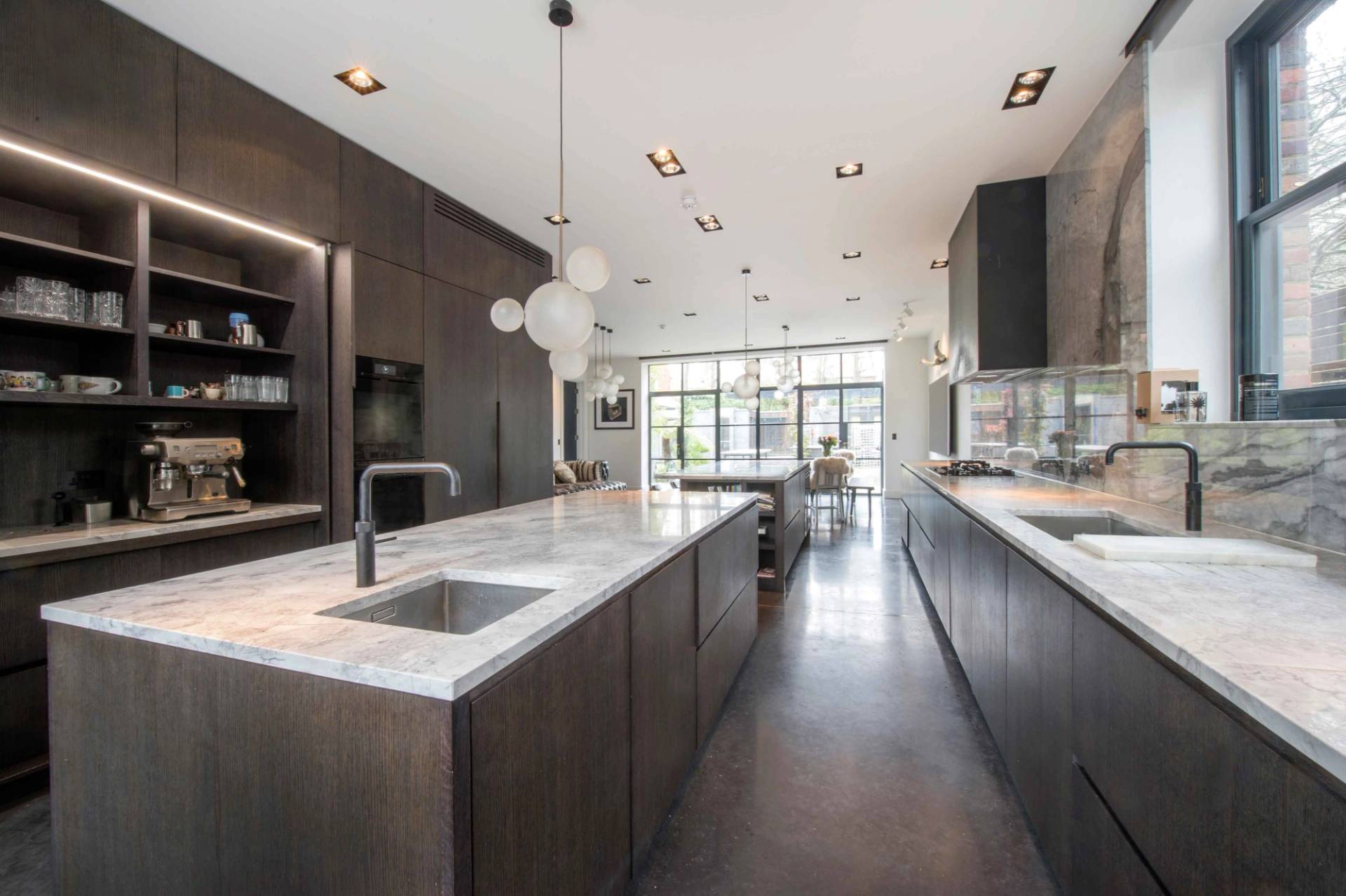 Sleek kitchen preparation area with premium stainless steel appliances, dark wood finish, and recessed ceiling lighting, Love Locations.