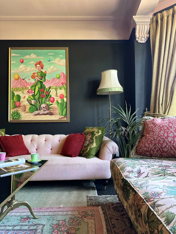 Moody dark blue reception room with pink tufted sofa, floor lamp, and eclectic wall art, Love Locations N13.