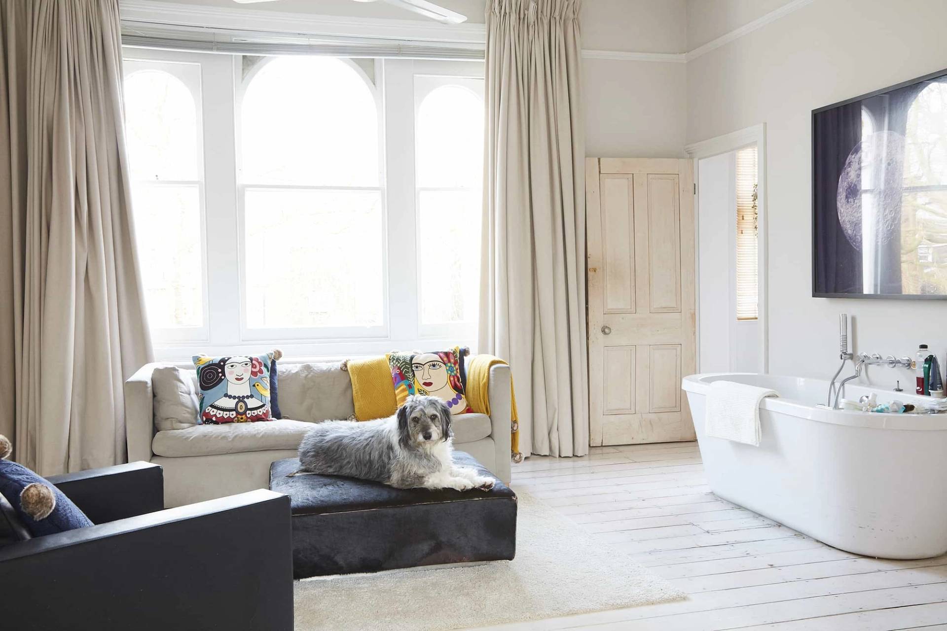 Spacious master bedroom featuring a white freestanding bathtub set directly on white painted floorboards beside a sash window, Love Locations.