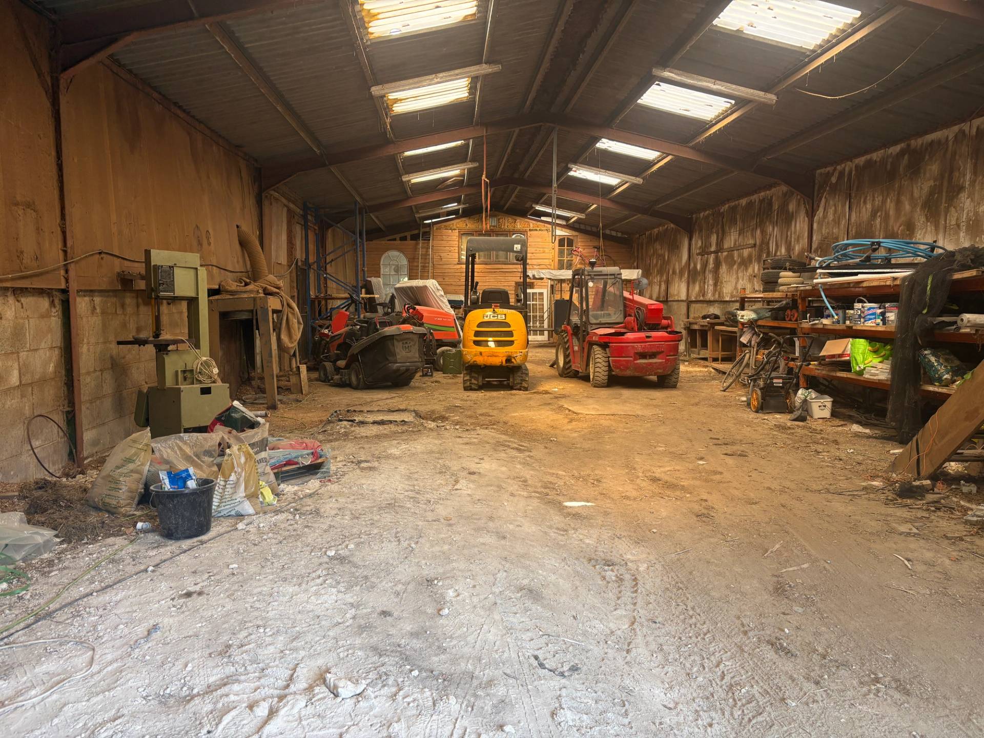 Large industrial farm workshop interior with steel roof trusses, skylights, concrete floor, machinery, and forklifts in South Chailey, Love Locations BN8.