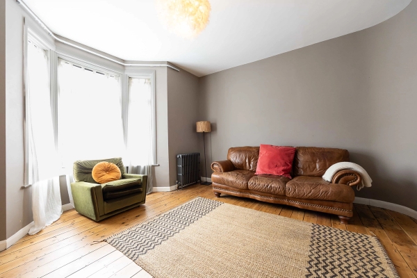 Love Locations period home lounge shoot space E7: Light-flooded reception room featuring a vintage brown leather sofa, a retro armchair, and original period windows, optimized for editorial photography.