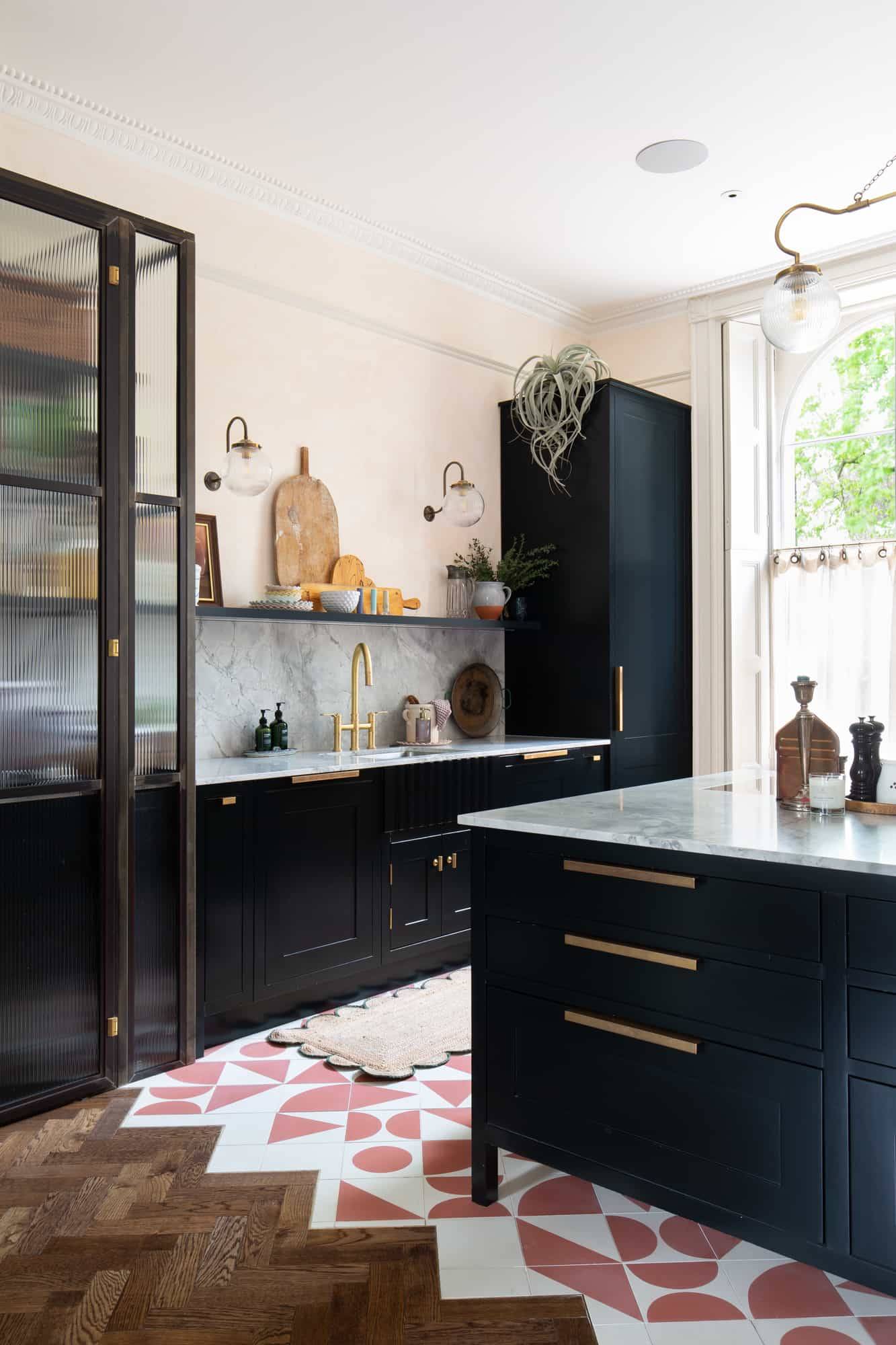 Close-up view of black kitchen cabinets with gold handles, marble worktop, and sash window light in Camberwell via Love Locations.