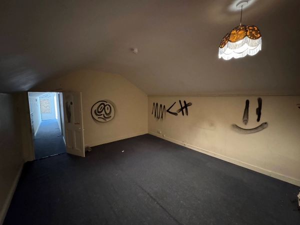 Eerie top-floor attic room setting with distressed beige walls and minimal black spray painted tags, curated by Love Locations.