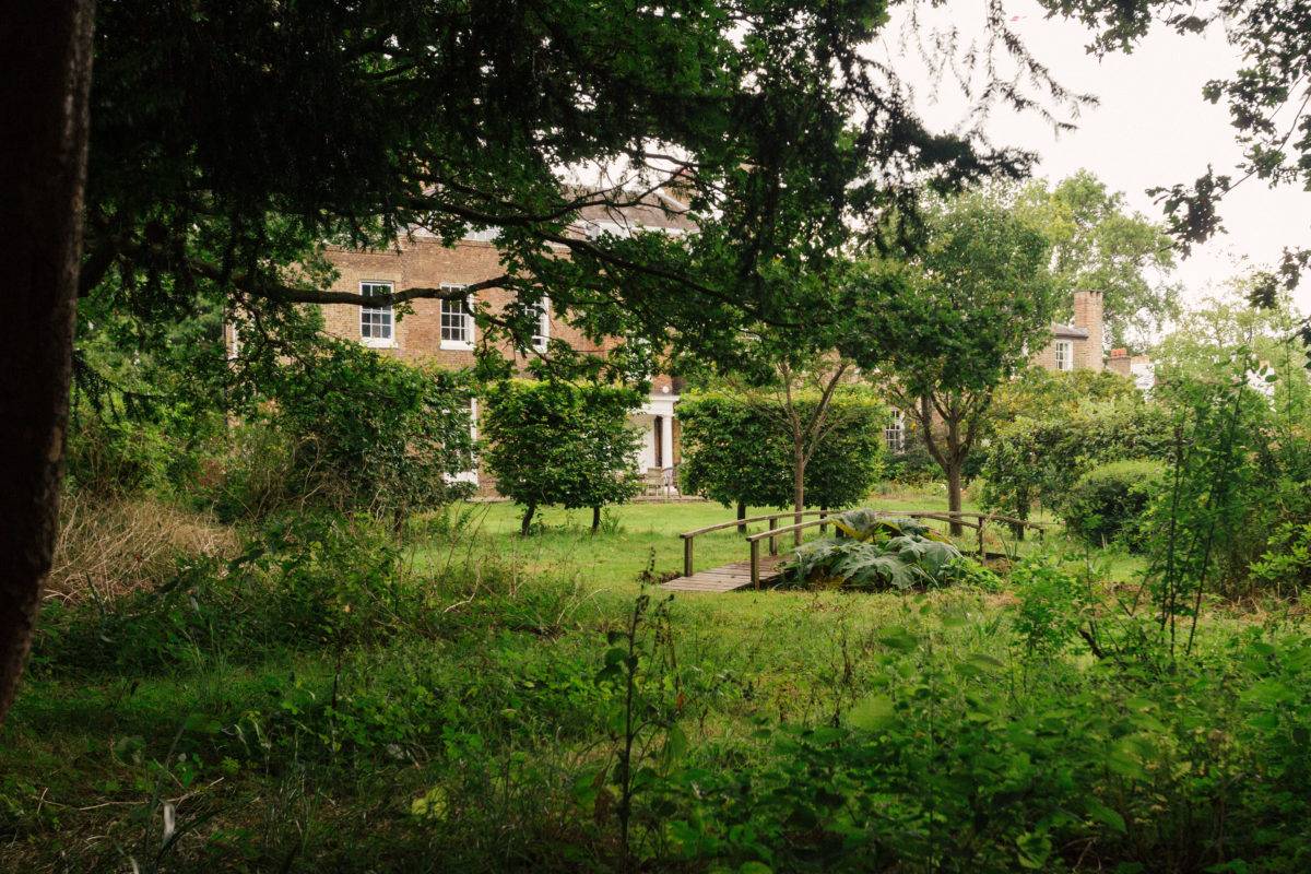 Manicured lawn garden with square-trimmed hedging trees set before a brick estate house, Love Locations.