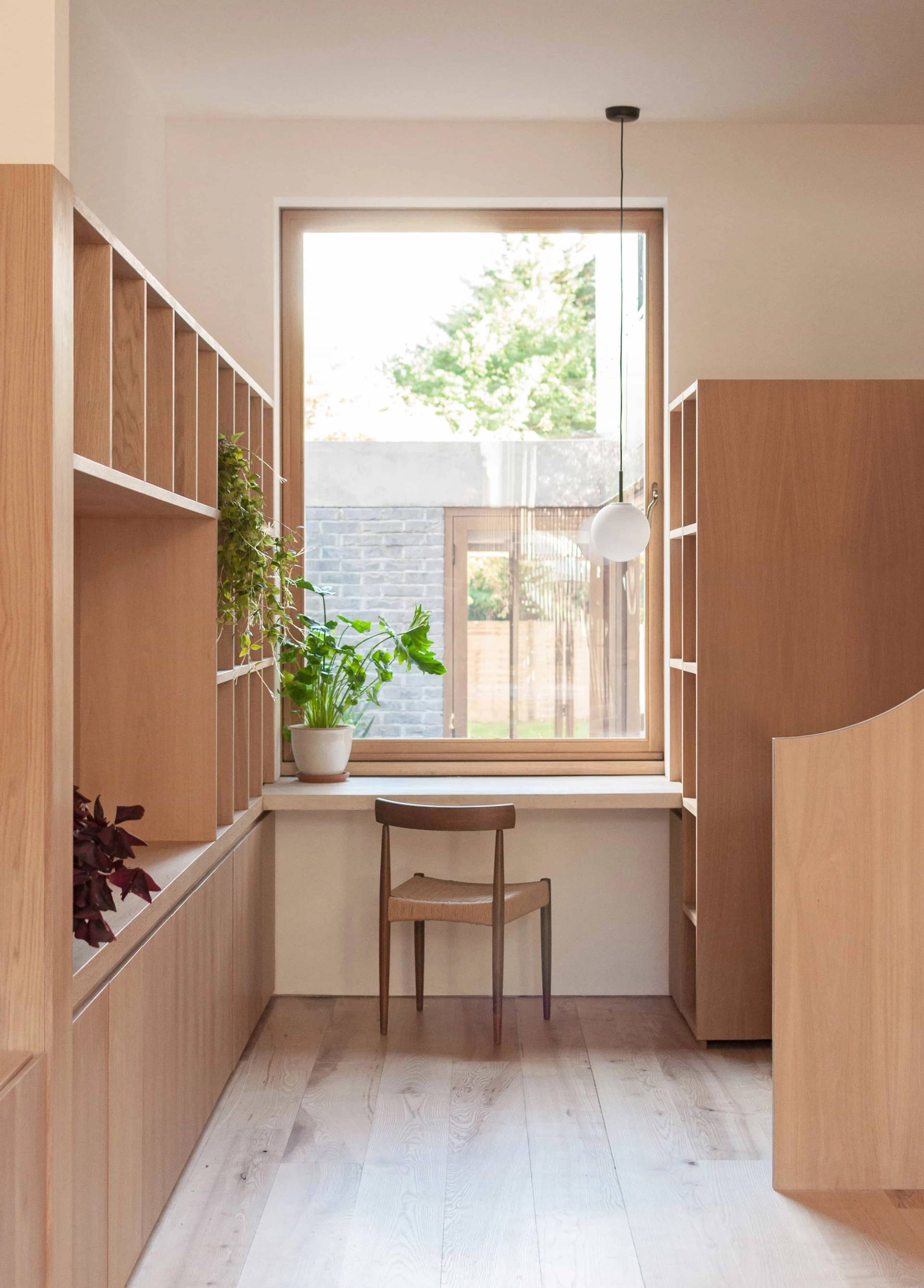 Custom home office study nook in Hackney N16 via Love Locations, featuring built-in oak shelving, a wooden desk, and a window overlooking an internal courtyard.