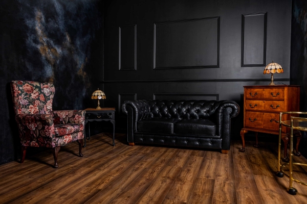Moody black studio room featuring dark wall mouldings, black leather chesterfield sofa, and vintage floor lamp, Love Locations N15.