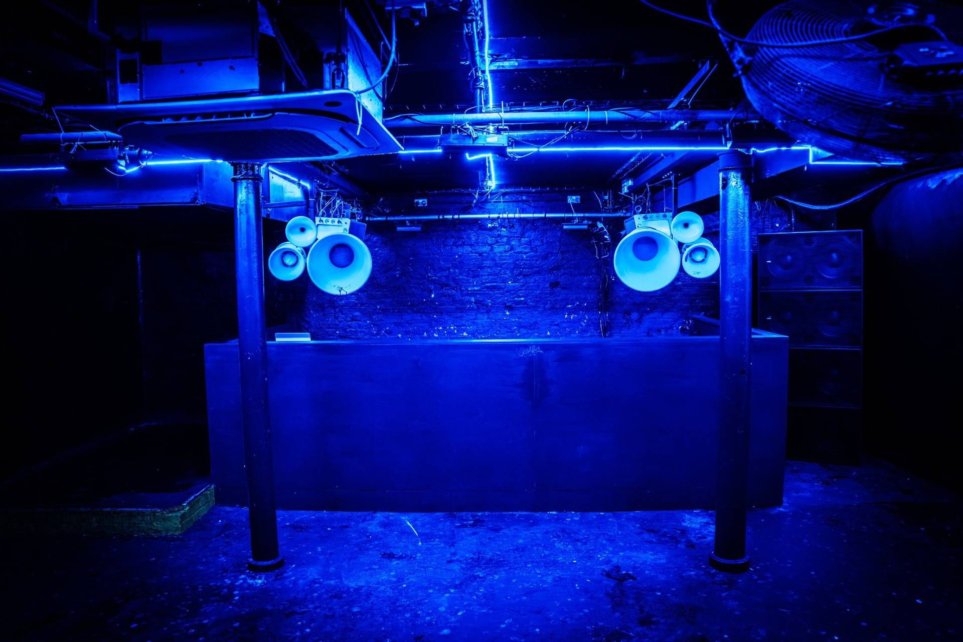 DJ booth and sound system setup framed by cobalt blue neon tube lighting in a Cheetham Hill production location through Love Locations.