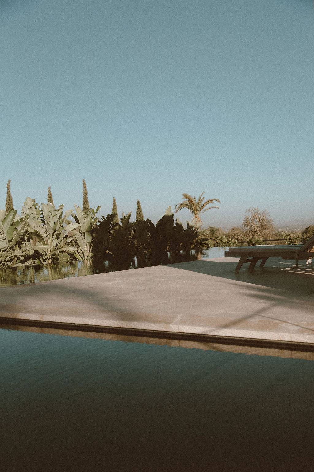 Sleek infinity pool deck with smooth stone paving looking towards a horizon under clear skies, Love Locations 07630.