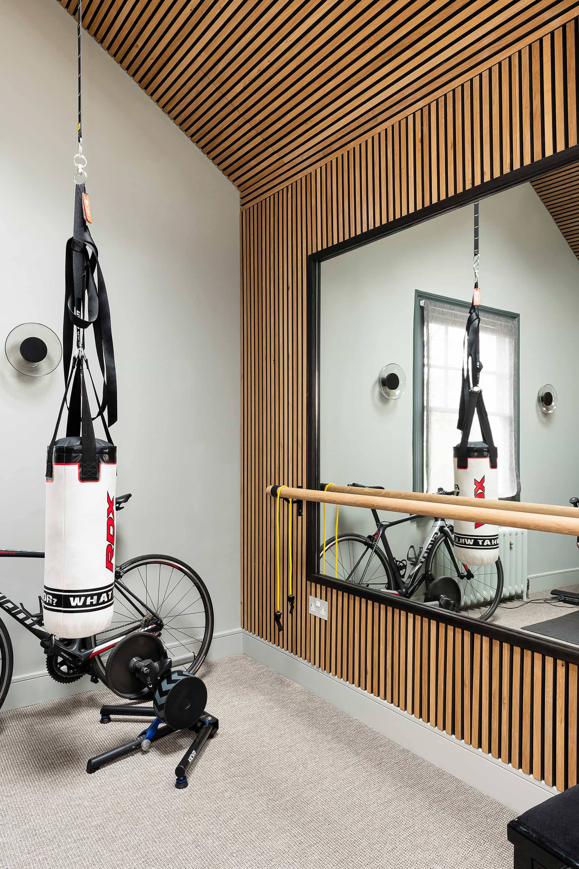 Home gym studio featuring slatted wood wall panelling, hanging punching bag, TRX straps, and large wall mirror, perfect for fitness brand advertising, Love Locations.