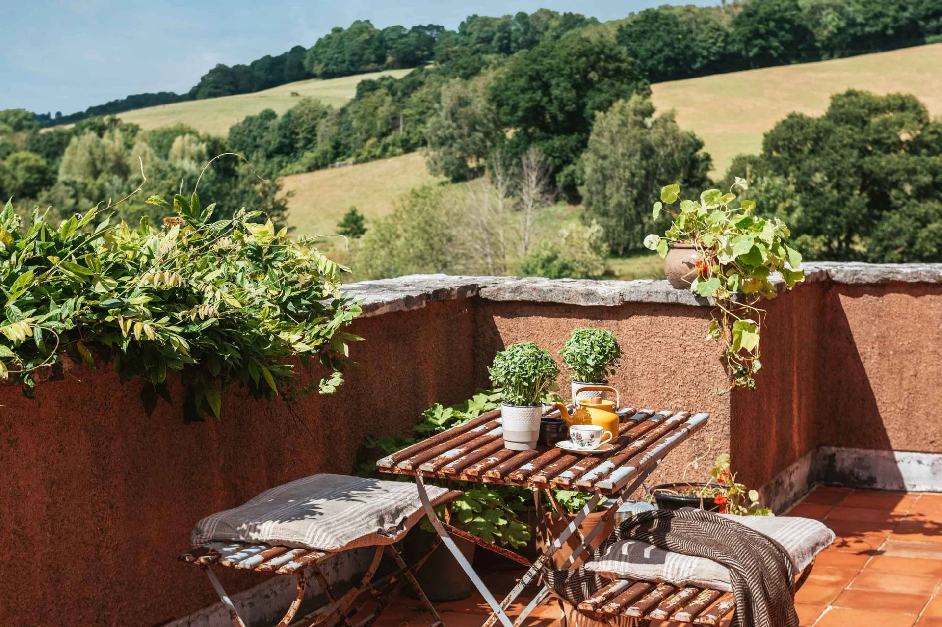Private outdoor balcony terrace with a wooden dining table looking out across rolling green Devon hills by Love Locations.