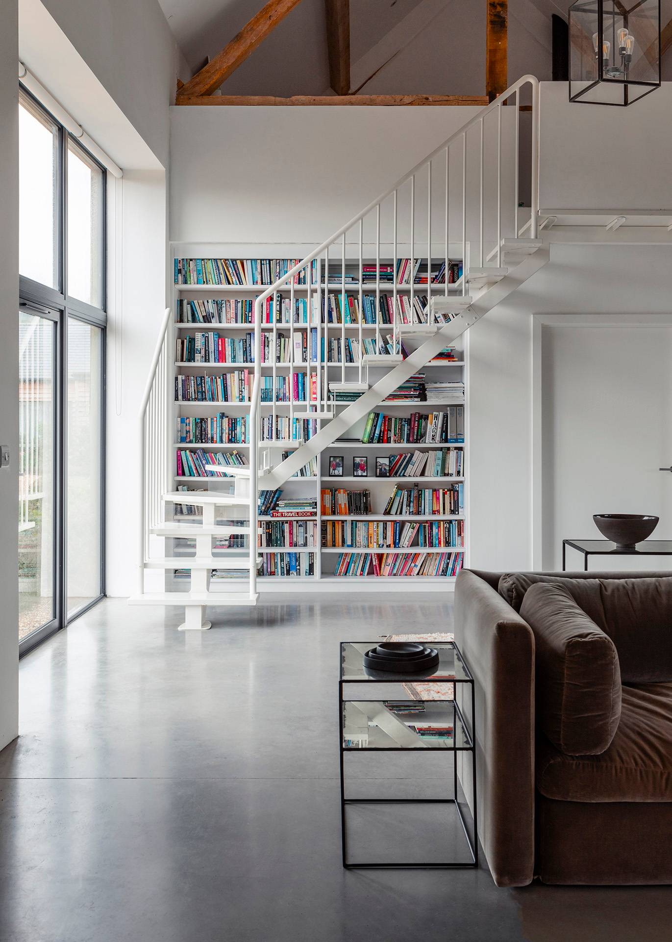 Full-height library bookcase wall set beside a white spiral staircase and polished concrete floors, Love Locations SN8.