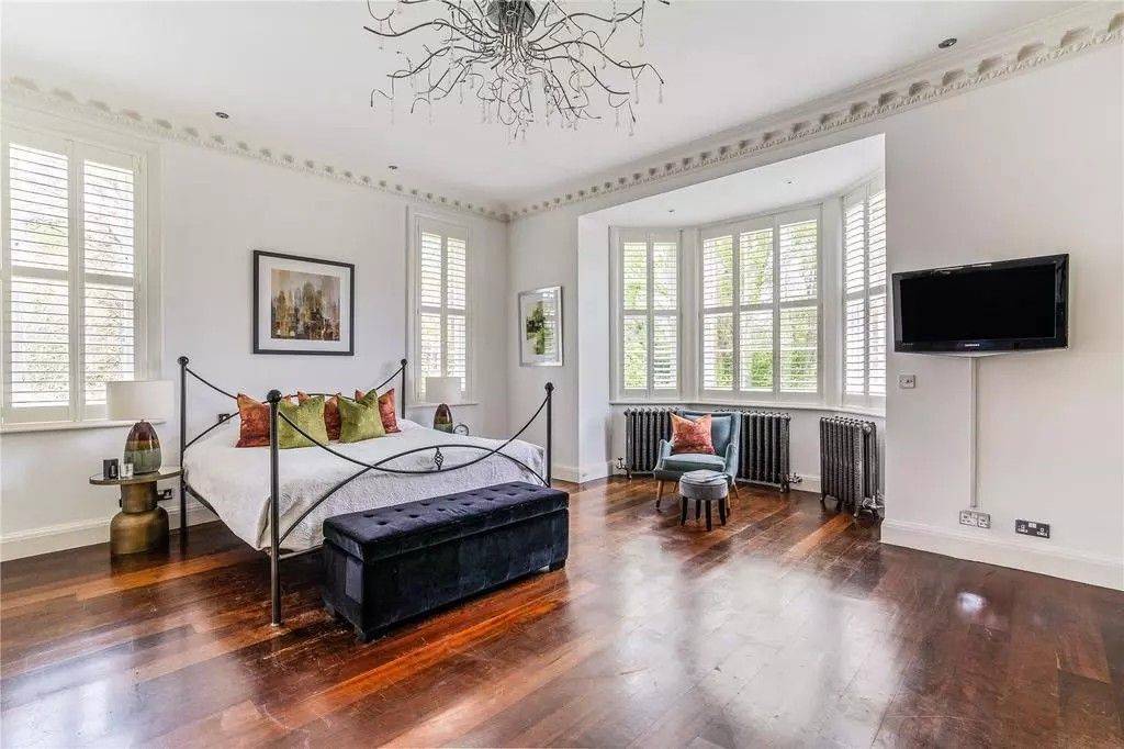 Light-filled bedroom shoot space featuring a wrought-iron bed frame, deep blue velvet ottoman bench, and classical bay windows by Love Locations.
