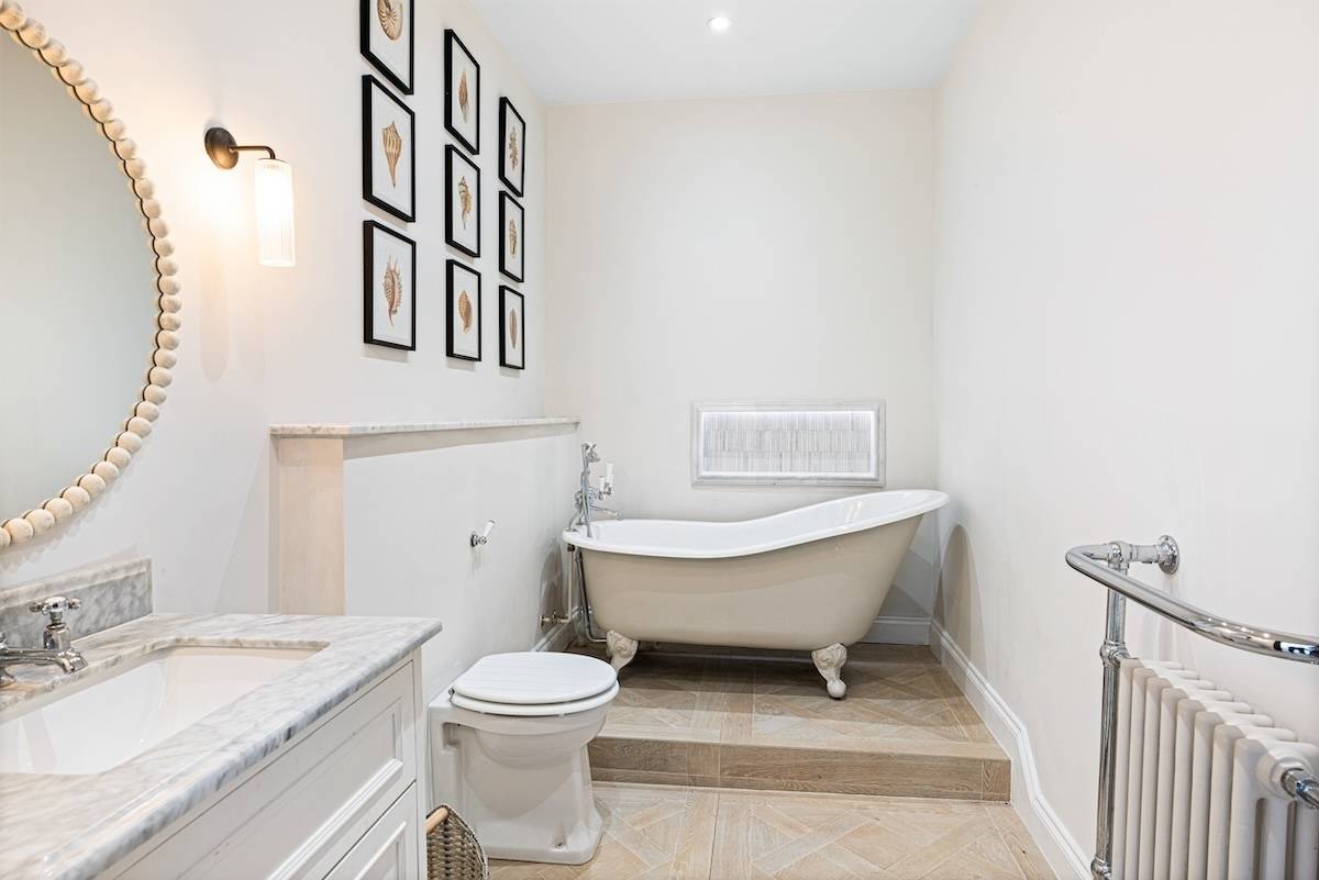 Spacious bathroom featuring a clawfoot bathtub, elevated tiled platform, and white pedestal sink, Love Locations RH13.
