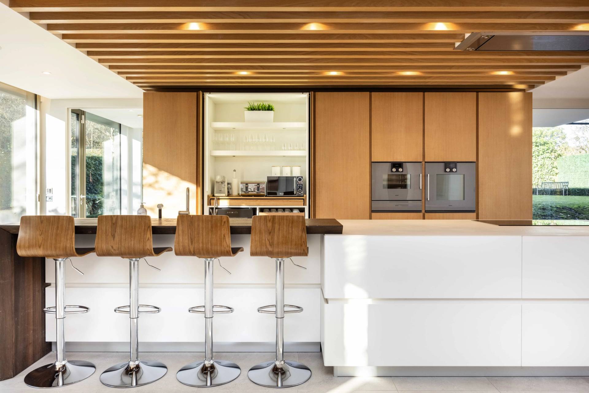 Close-up view of chrome kitchen bar stools set against a white island with timber slatted ceiling detail, Love Locations WD7.
