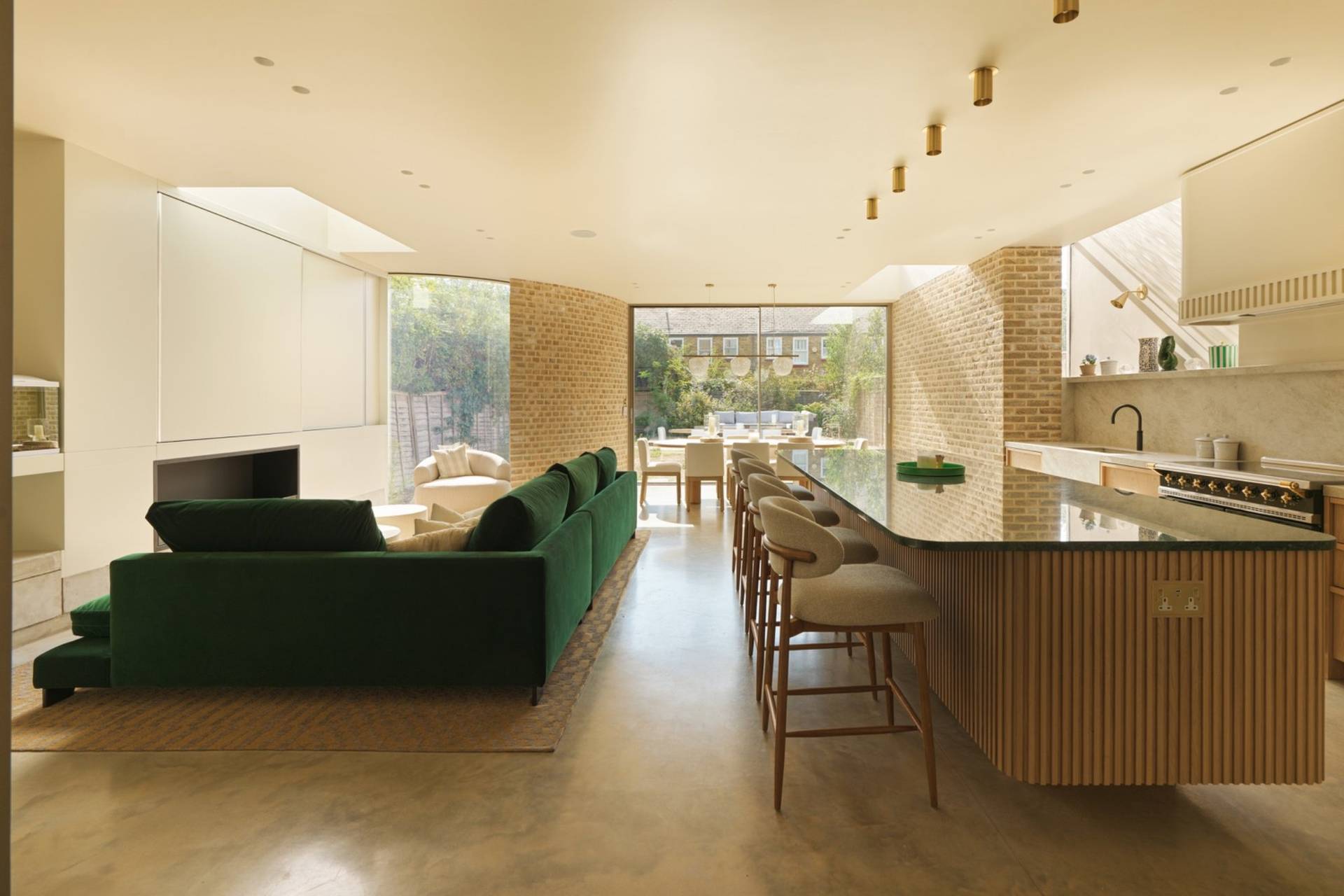 Sprawling open-plan contemporary living room and kitchen film location in Clapham South SW11 from Love Locations, featuring polished concrete floors, forest green velvet sofa, and a fluted timber kitchen island.