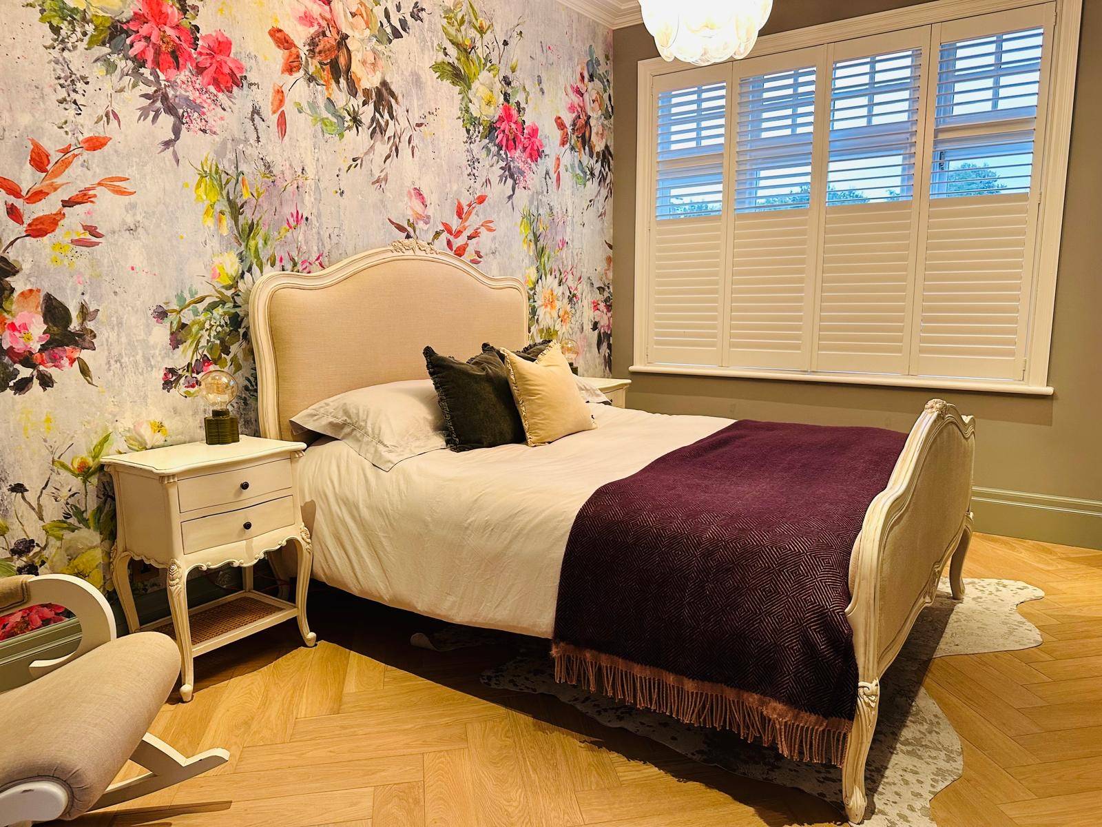 Luxury bedroom with colorful floral wallpaper backdrop, upholstered headboard, and brass sconces, Love Locations TW11.