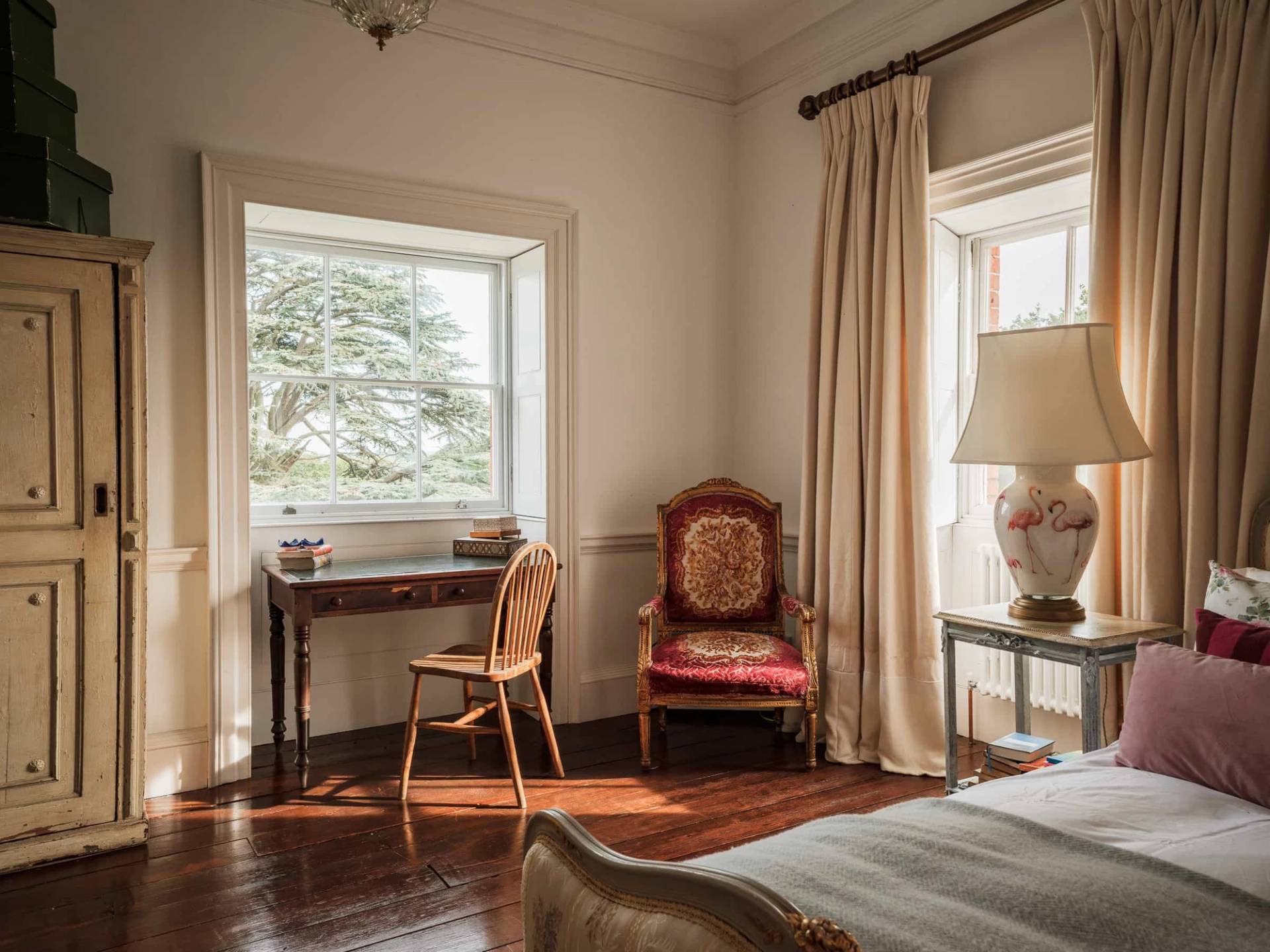 Bedroom seating corner featuring a wooden writing desk, red leather chair, and sash window curtains, Love Locations RG42.