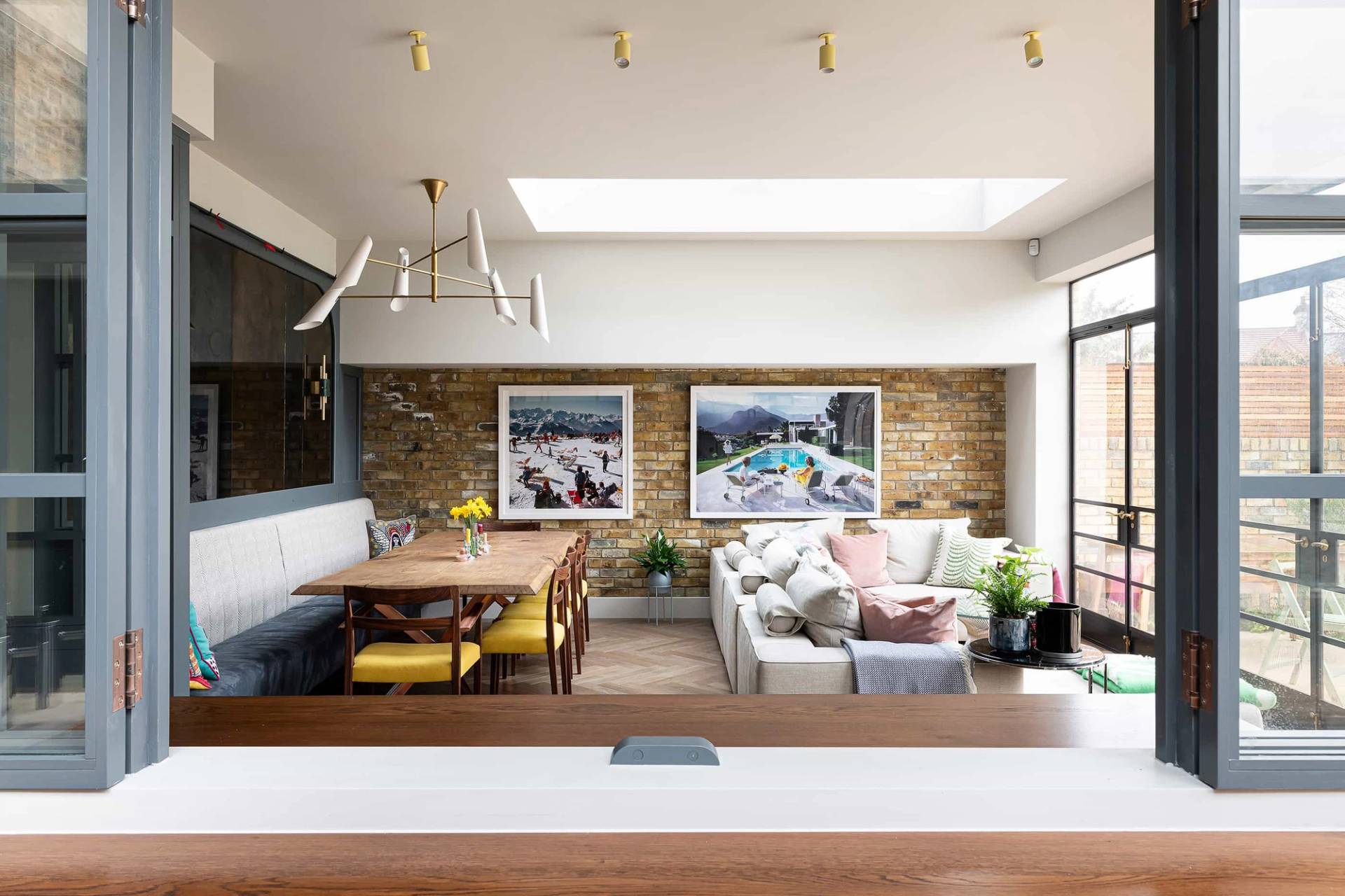 Spacious open-plan living and dining room extension with exposed yellow stock brick walls, skylights, and herringbone parquet flooring, perfect for family brand advertising, Love Locations NW6.
