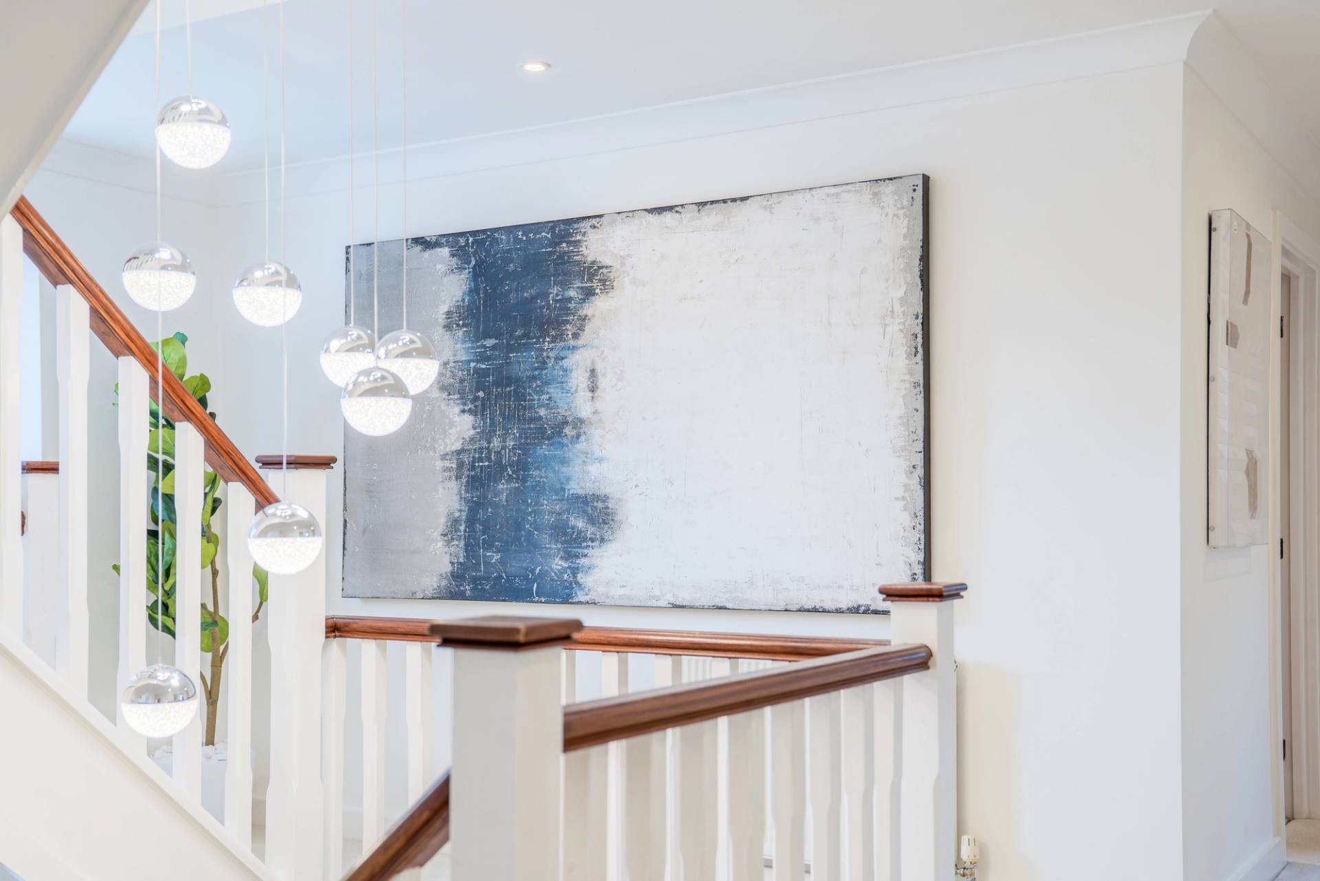 Upper landing gallery wall featuring abstract artwork framed by white staircase balustrades, Love Locations RM11.