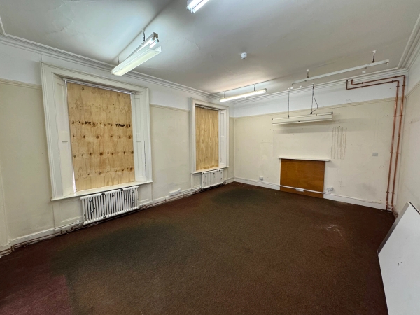 Derelict institutional room with tall boarded-up windows and industrial strip lighting for gritty music video shoots, listed by Love Locations.