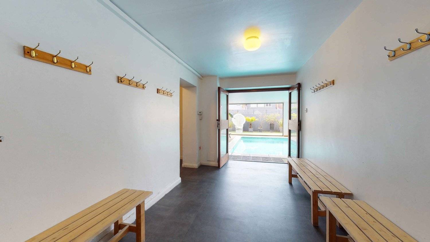 Indoor swimming pool changing room transition with wooden benches and dark slate flooring, Love Locations SW16.