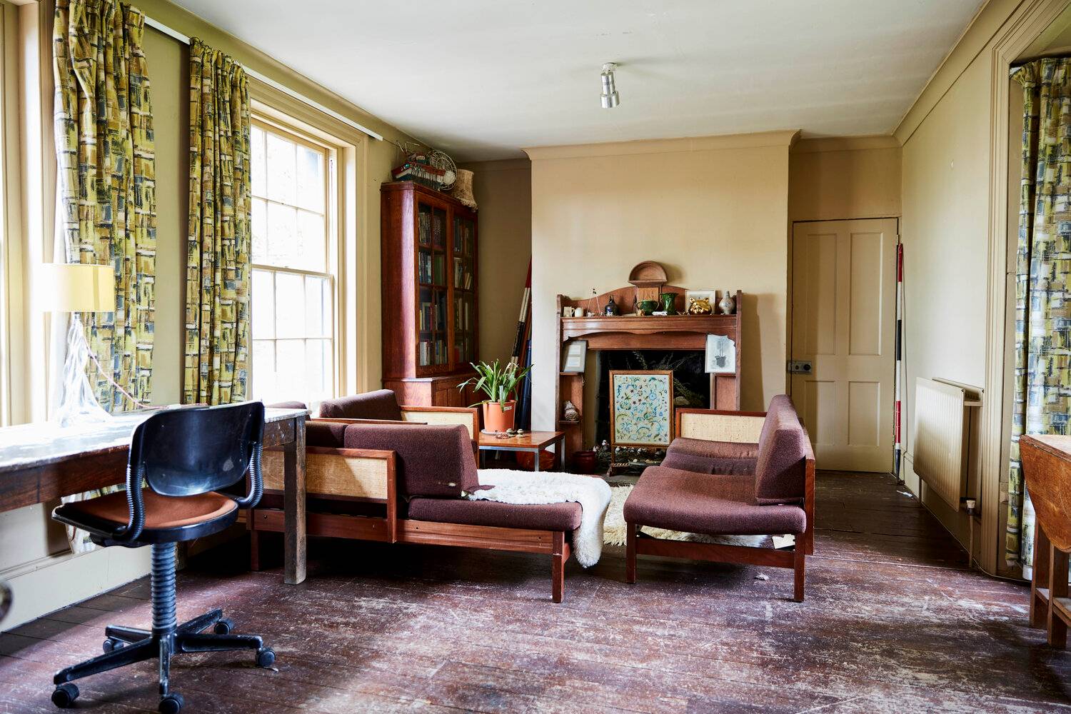 Mid-century modern lounge featuring a wood-burning stove fireplace, teak armchairs, and original sash windows, Love Locations.