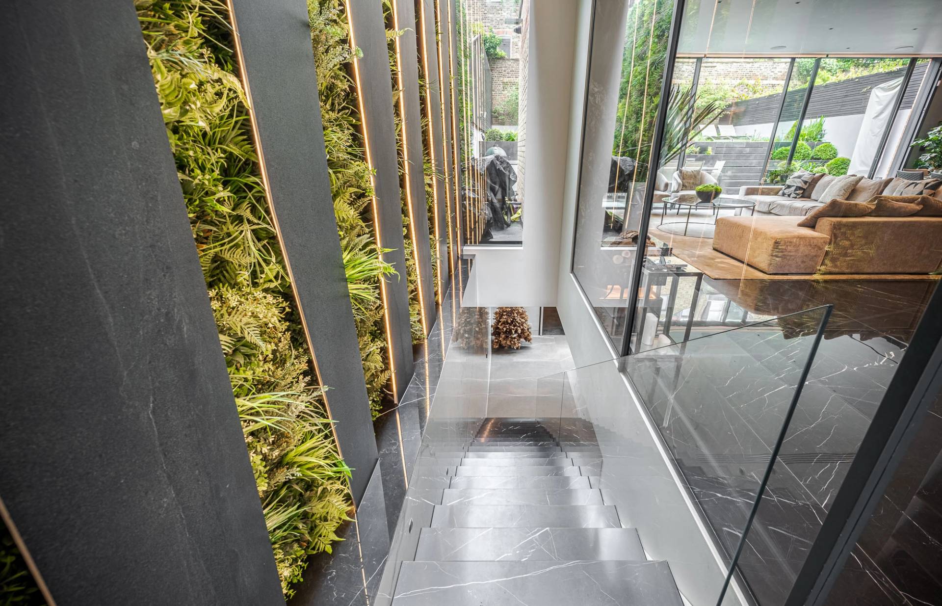 High-angle view of a indoor vertical plant wall set beside a basement lightwell and glass balustrades, Love Locations SW11.