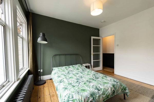 Love Locations green master bedroom shoot location Forest Gate E7: Creative bedroom with a deep sage green accent wall, black metal bedframe, and tropical palm bedding, perfect for lifestyle brand shoots.