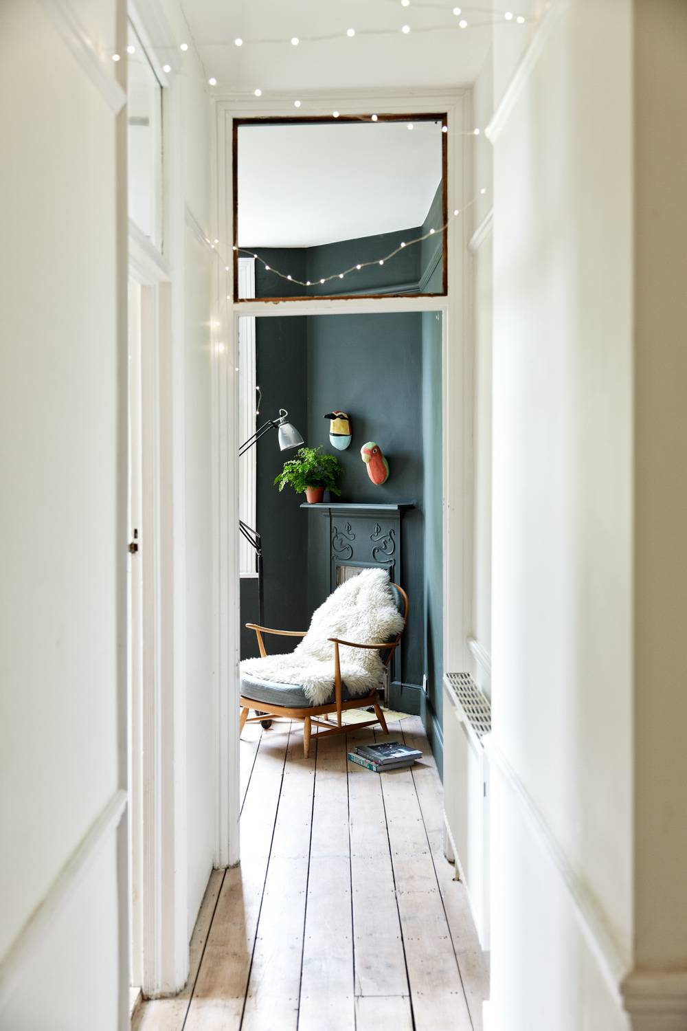 View through a bright hallway doorway into a moody dark teal study room with a vintage armchair, Love Locations N13.