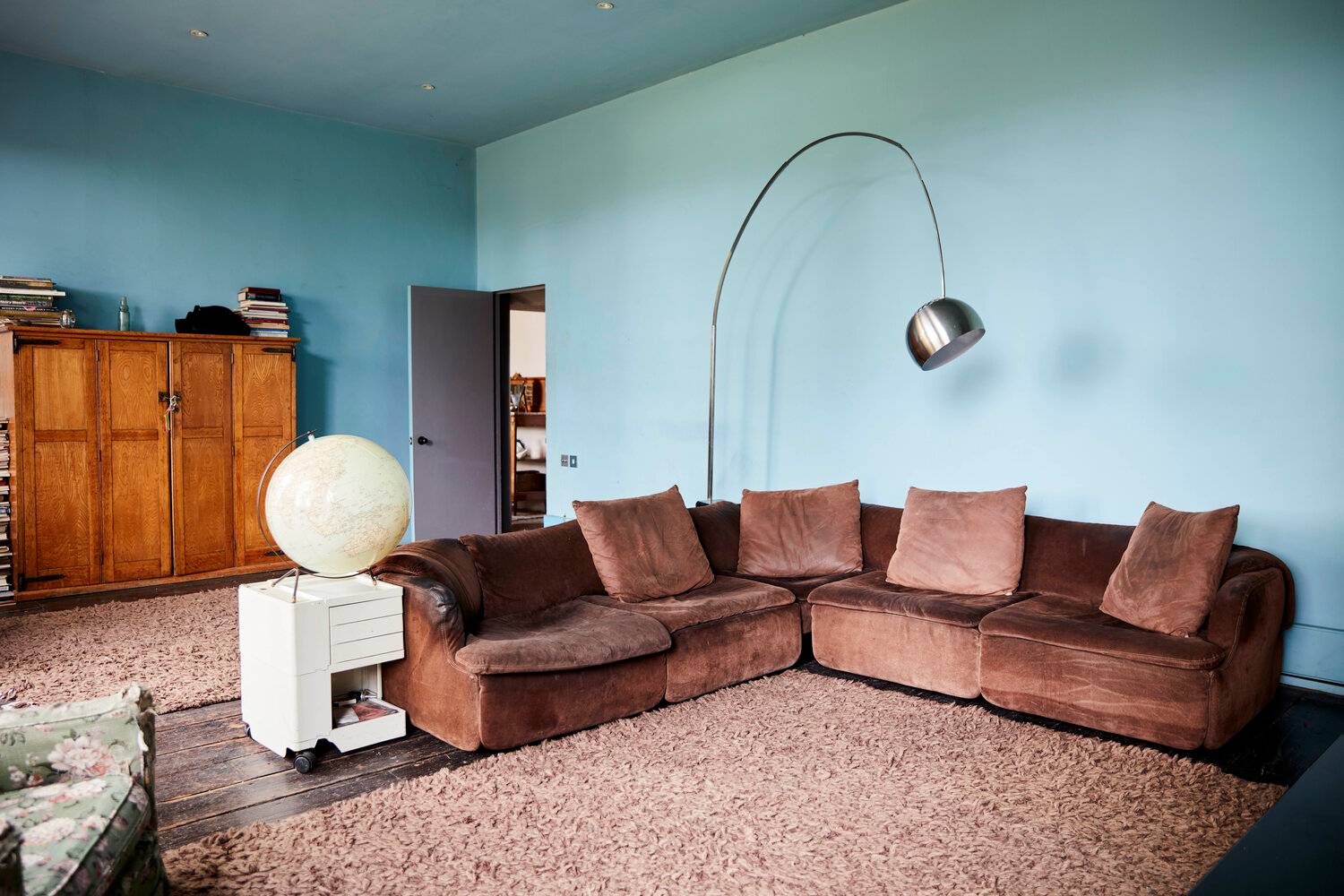 Bright blue living room with a brown velvet sofa, plush carpet, and modern floor lamp, Love Locations.