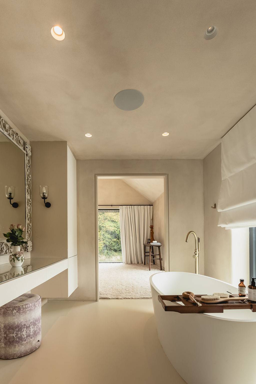Open-plan bathroom suite view showing a freestanding tub looking through to a light-filled bedroom, Love Locations GU32.
