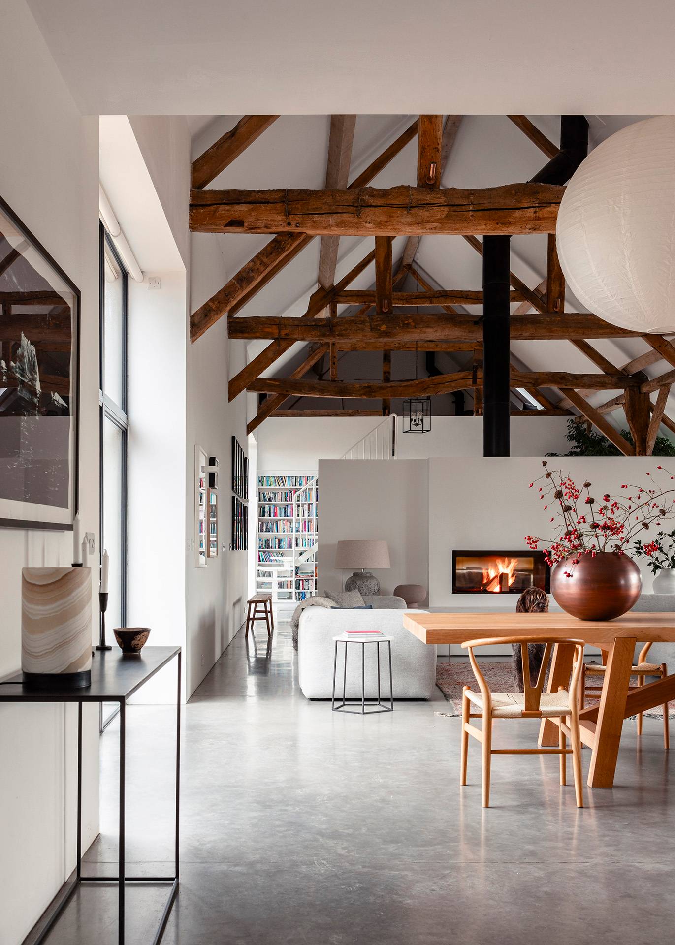Vaulted timber-framed barn conversion shoot location in Wiltshire, SN8 featuring polished concrete floors, open-plan dining table, and modern hearth via Love Locations.