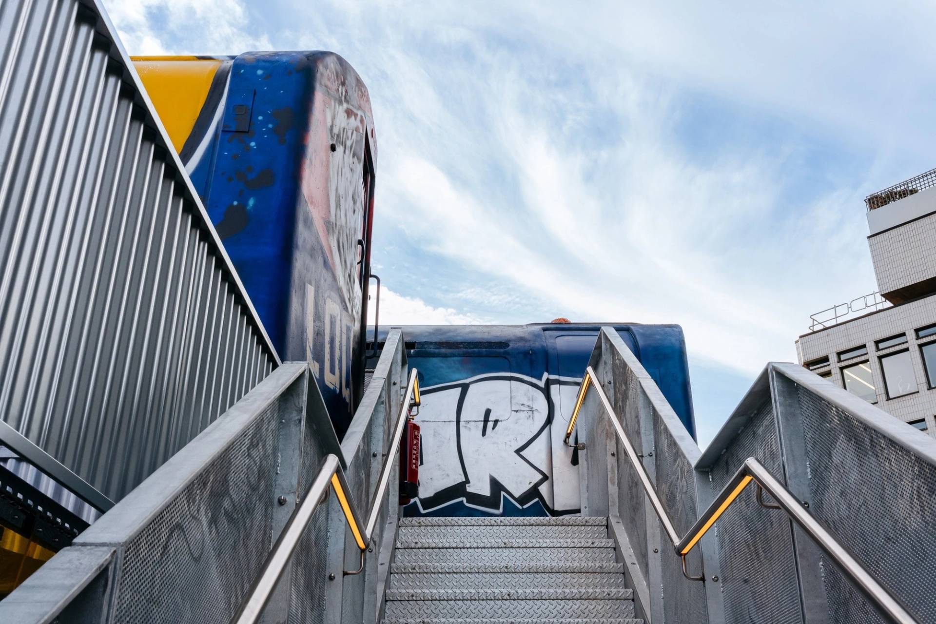 Metal staircase leading up to graffiti-covered vintage train carriages converted into event spaces in Hackney EC2A via Love Locations.
