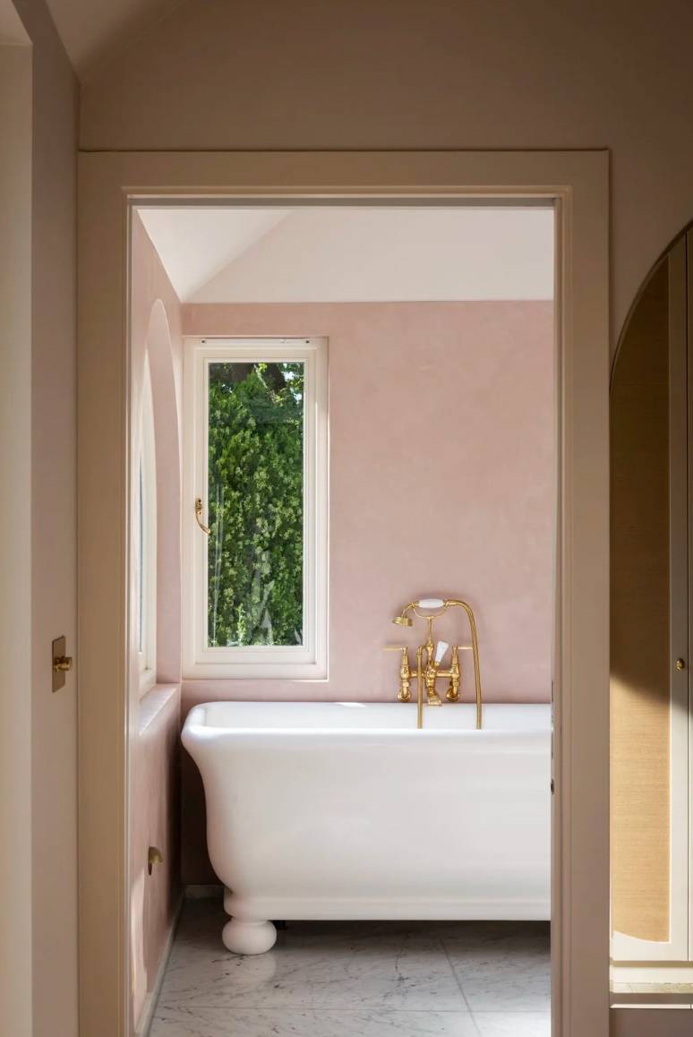 Spacious master bathroom featuring soft pink plaster walls, a white soaking tub, and brass tapware, ideal for skincare commercial shoots, Love Locations.