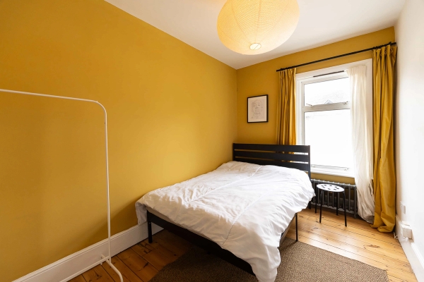 Love Locations vibrant yellow bedroom location E7: Cozy room decorated with a warm mustard yellow feature wall and simple black double bed, a colorful background for youth or lifestyle branding.
