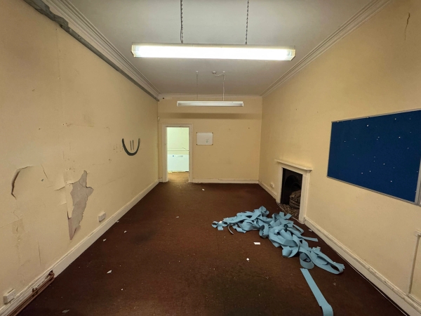 Long shot of an unmodernised institutional hall featuring twin fireplace surrounds and peeling paint textures, Love Locations.