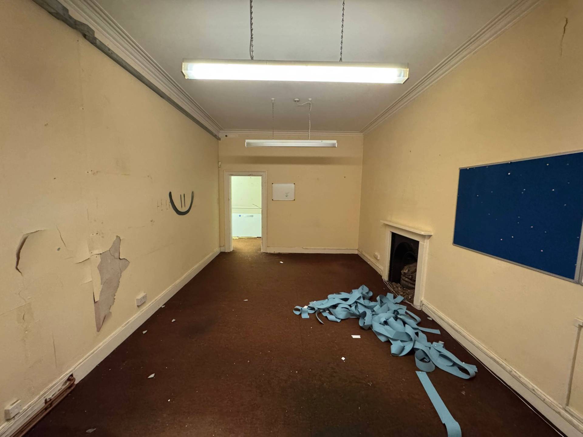 Long shot of an unmodernised institutional hall featuring twin fireplace surrounds and peeling paint textures, Love Locations.