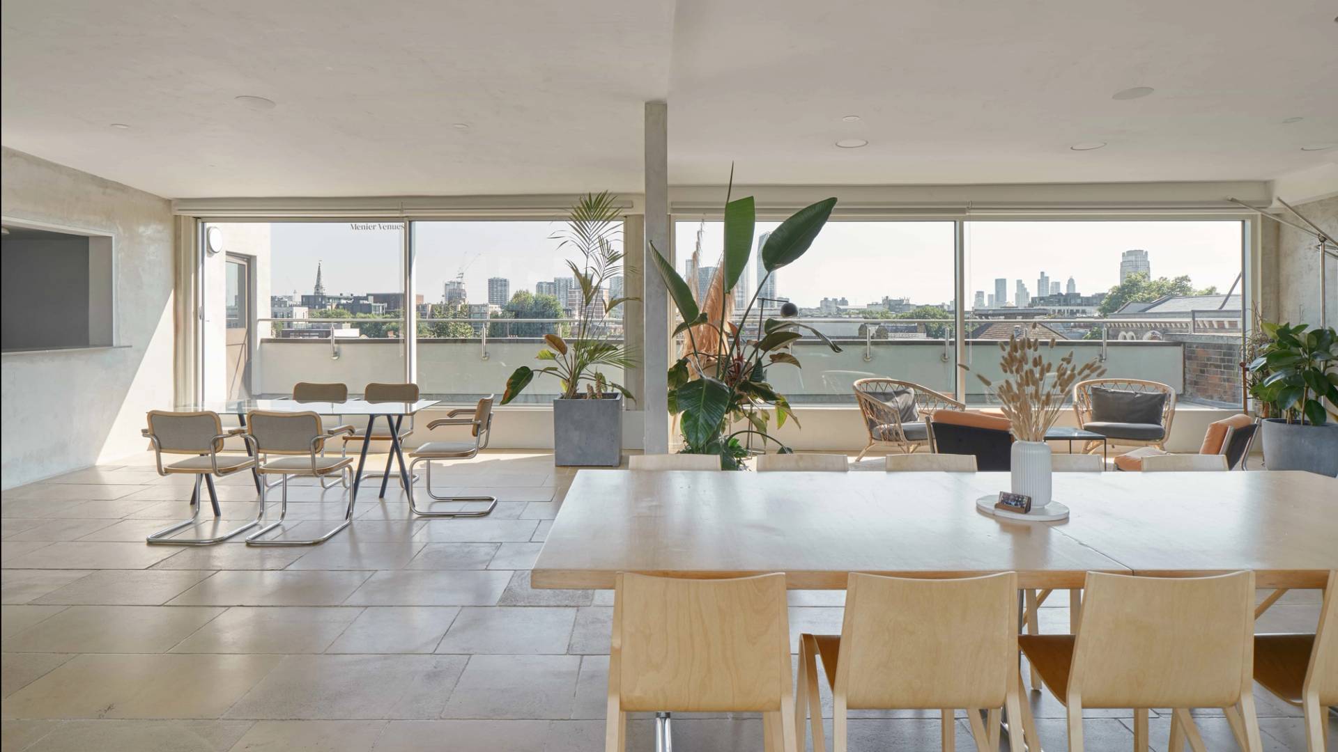 Spacious modern penthouse interior with floor-to-ceiling windows, large dining table, contemporary chairs, and lush indoor plants overlooking the London skyline at THE PENTHOUSE SE1.