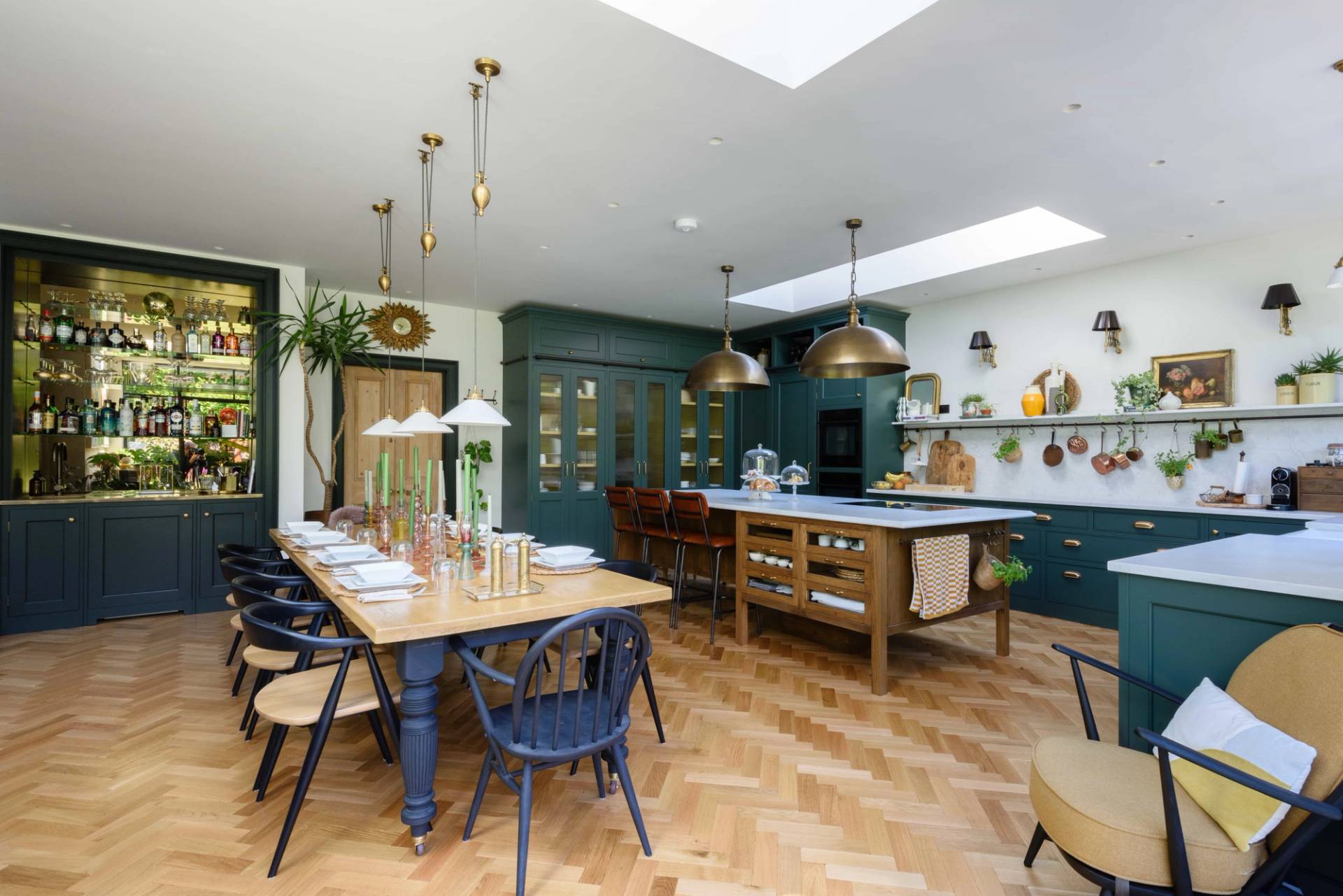 Forest green shaker kitchen and dining room with a long wooden dining table, brass pendant lights, and parquet flooring, Love Locations TW11.