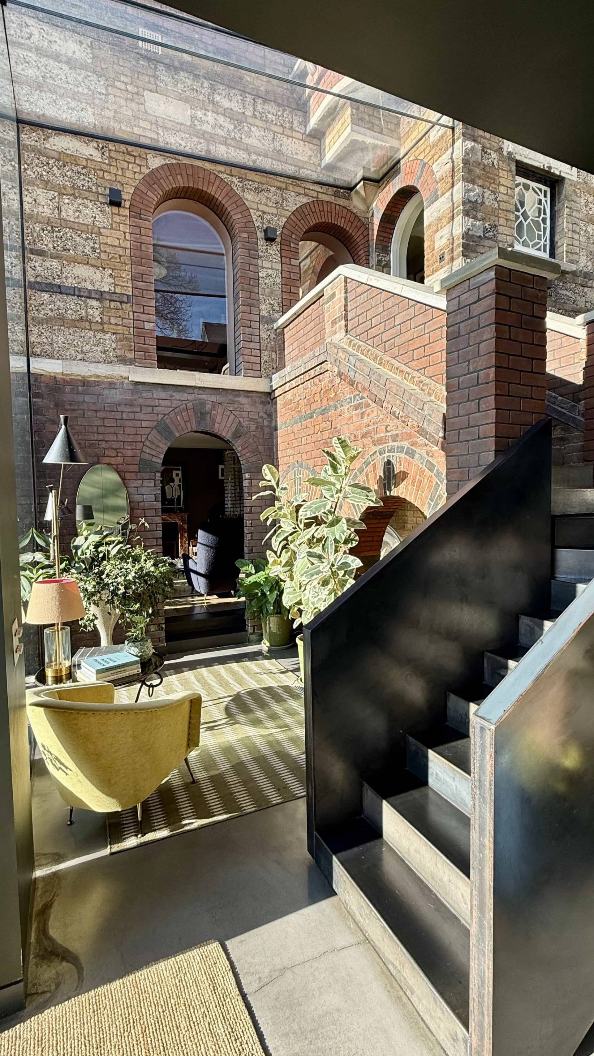 Character hall transition showing a black metal staircase set beside exposed brick archways and indoor potted plants, ideal for fashion editorial shoots, Love Locations SW20.