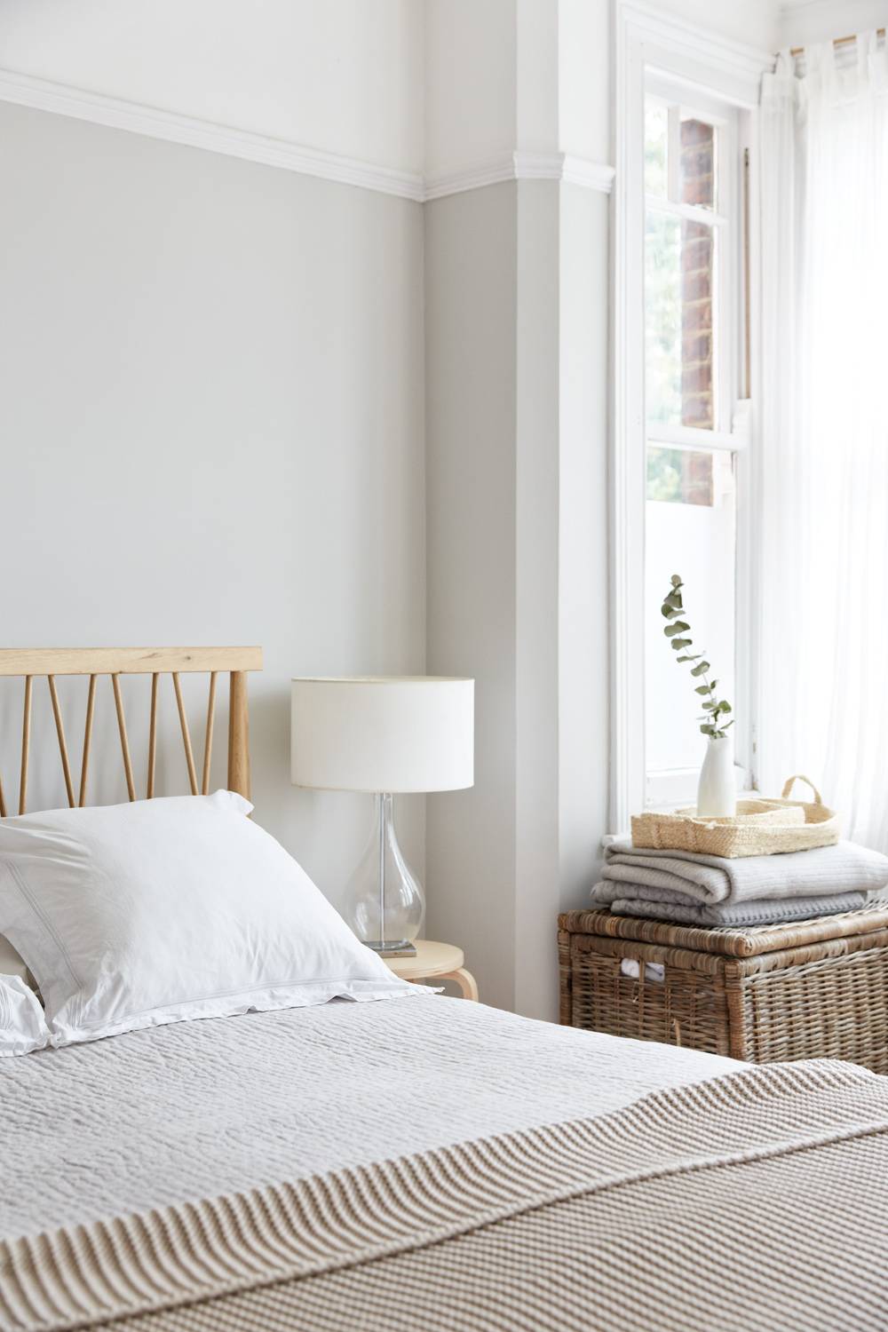Scandi bedroom corner with a light wood bed headboard, glass table lamp, and woven storage hamper, Love Locations N13.