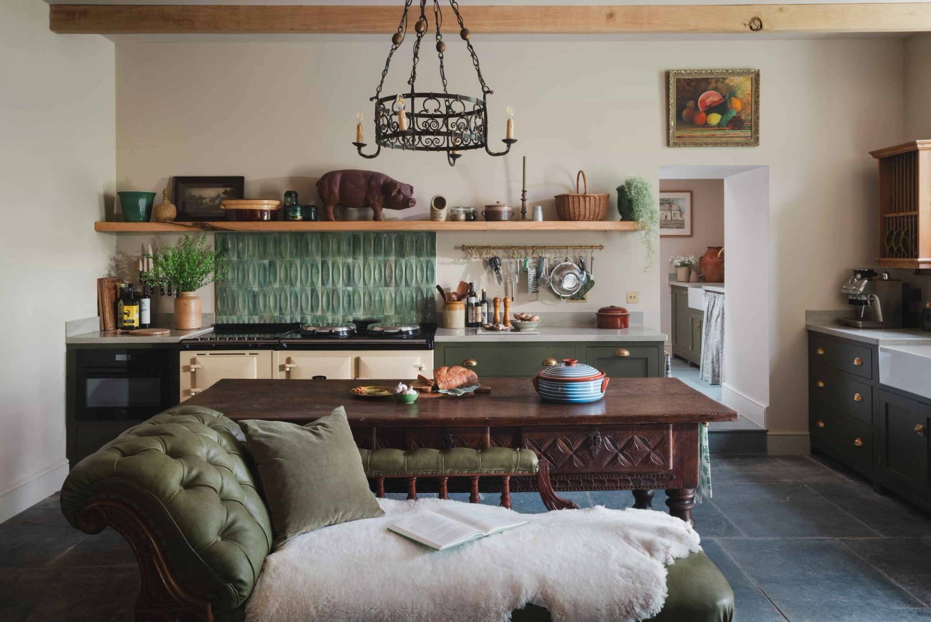 Rustic manor kitchen film location in Newquay Cornwall TR8 from Love Locations, showcasing green shaker cabinetry, an island counter, and a stone wall backdrop with a plush green sofa.